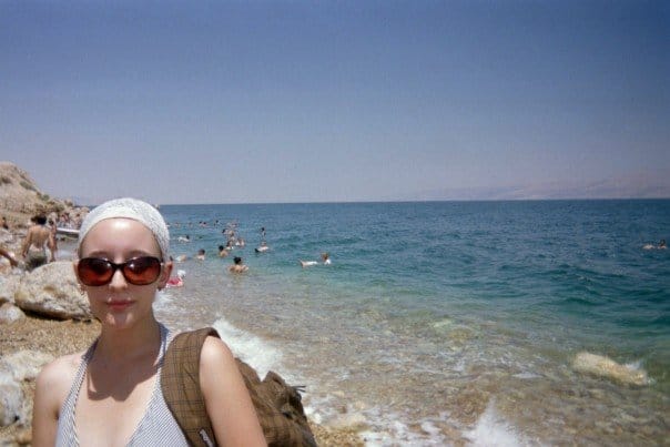 the author on a sunny beach in Israel twenty years ago, wearing big sunglasses and carrying a plaid backpack