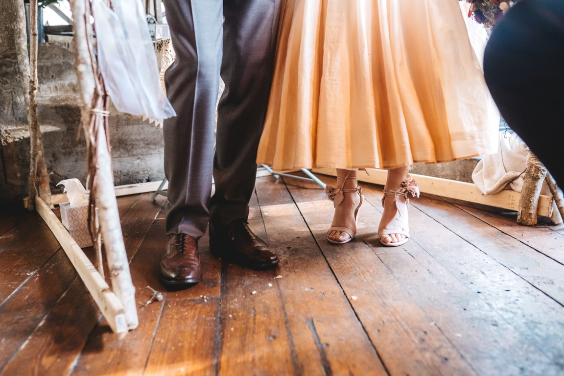 The beautifully shod feet of a handsome couple on a rustic wooden floor, the man in polished brown wingtips and the lady in fancy high-heeled pale tan strappy sandals