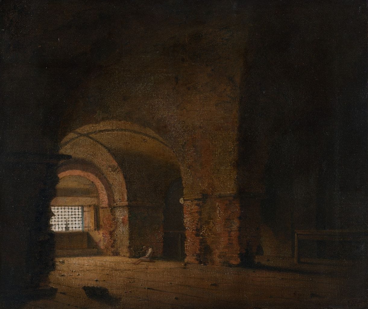 A lone figure, head bowed, seated on the floor of a dark prison cell with light filtering in through barred windows