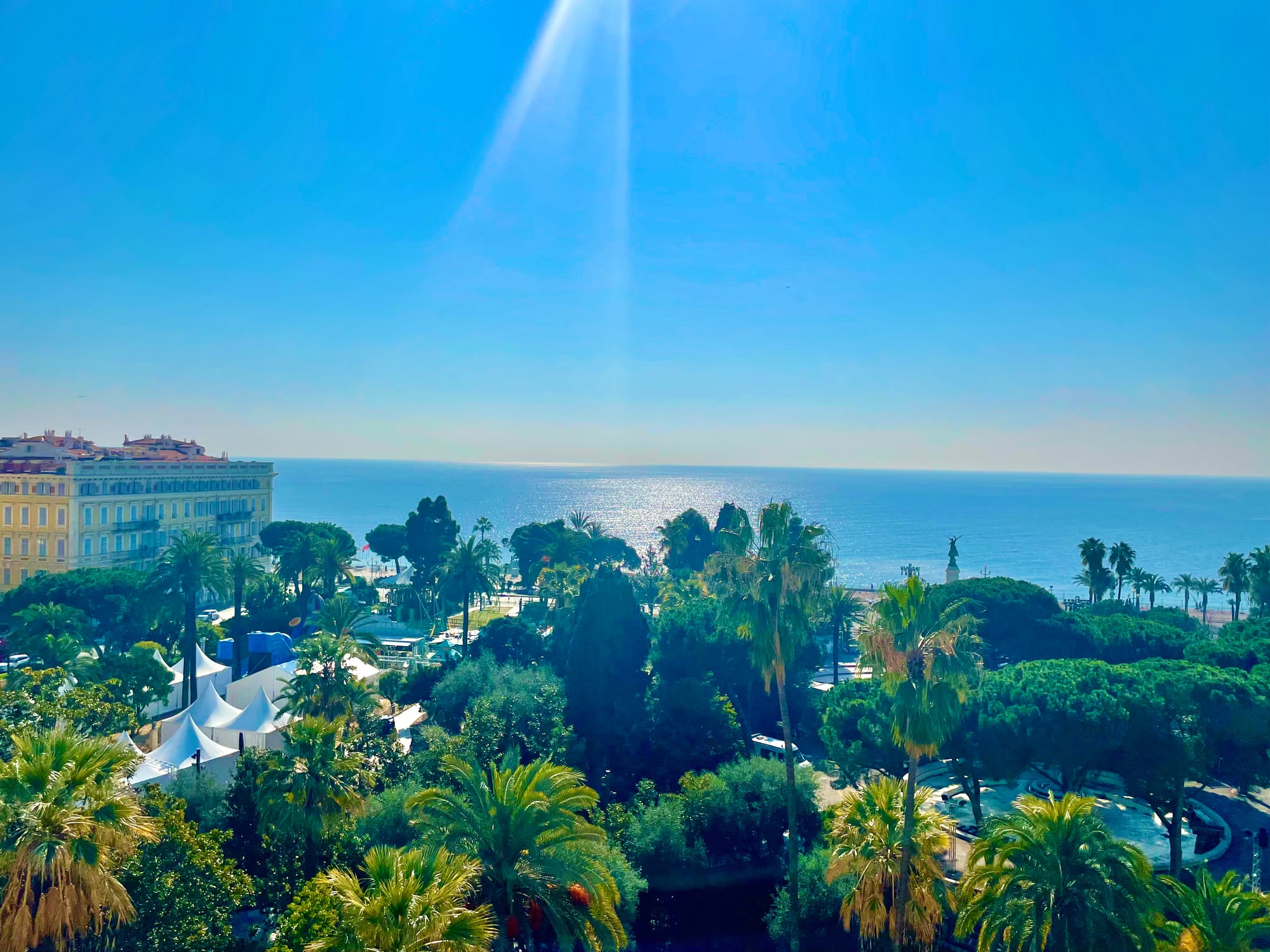 Breathtaking view of the Côte d'Azur from the Anantara Plaza Nice Hotel; lush evergreens and pine trees crowd a garden strip before the sparkling sea, like a Dufy painting come to life
