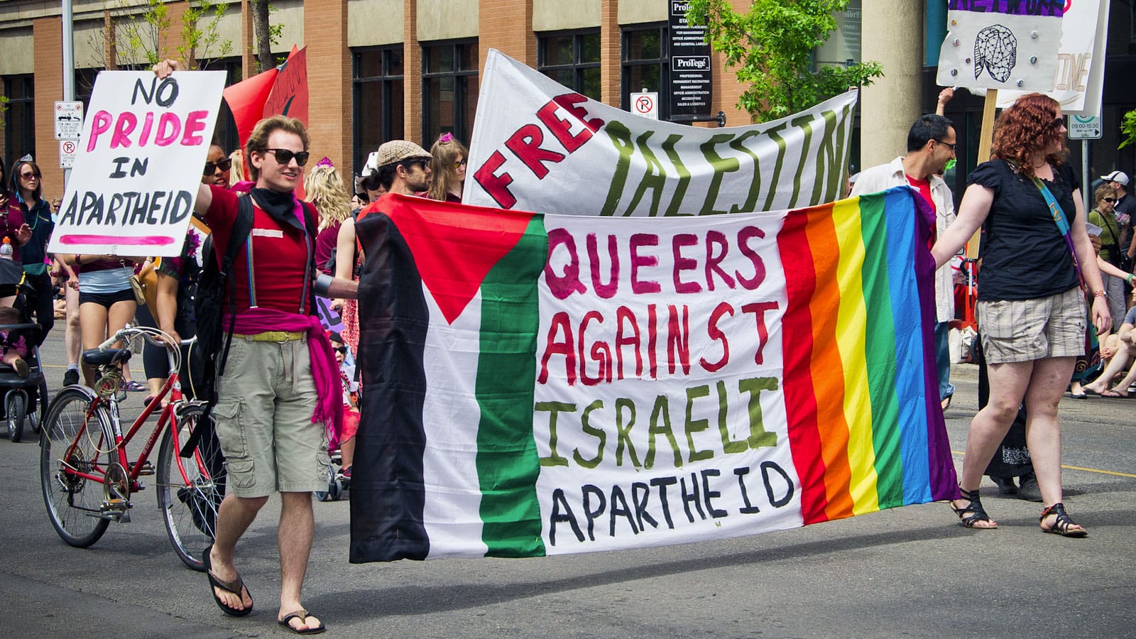 Edmonton Pride Parade 2011 photo shows colorful marchers with 'Queers Against Israeli Apartheid' and 'No Pride in Apartheid' banners banner