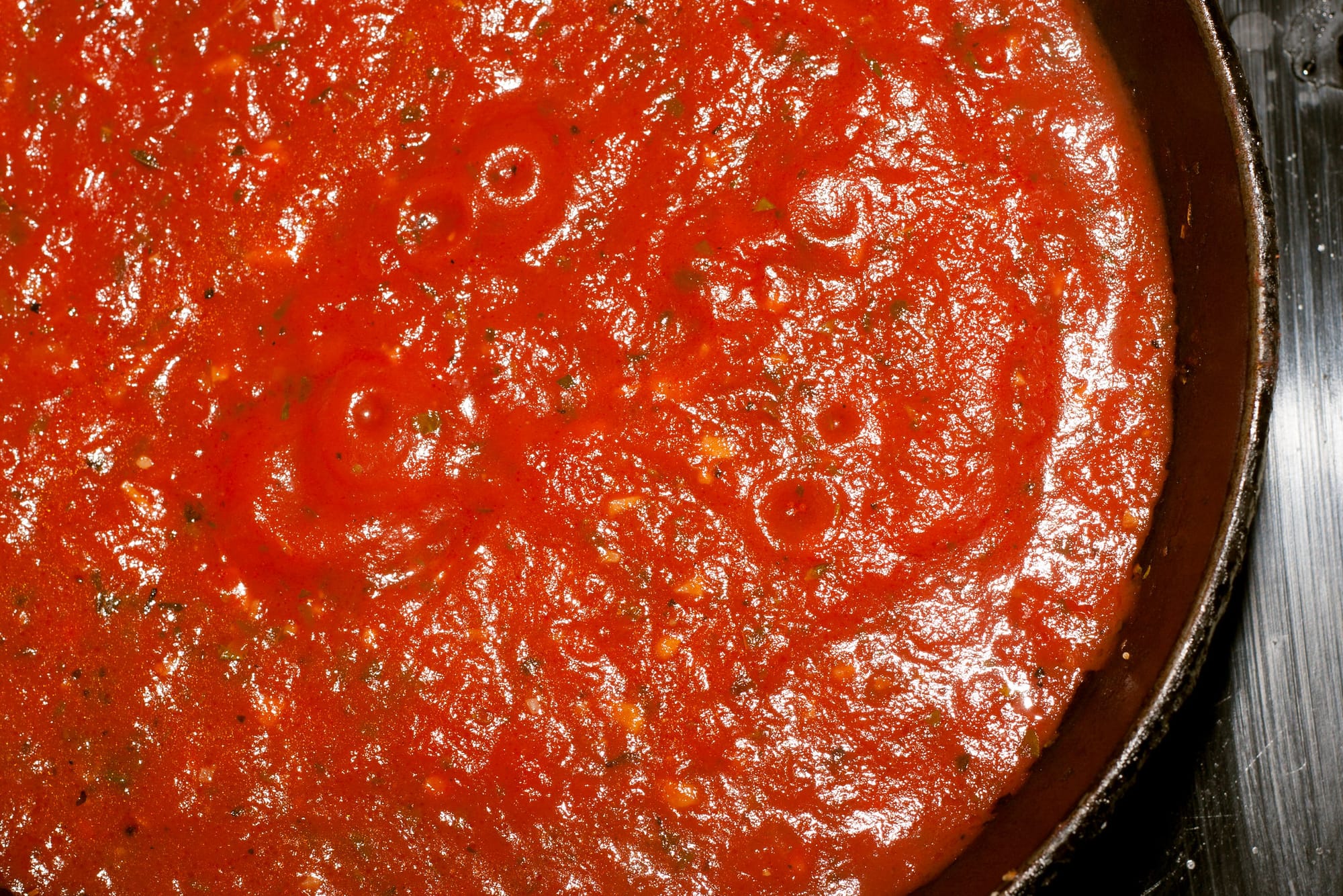Detail from above of a cast iron pot full of bright red tomato pasta sauce simmering on the hob