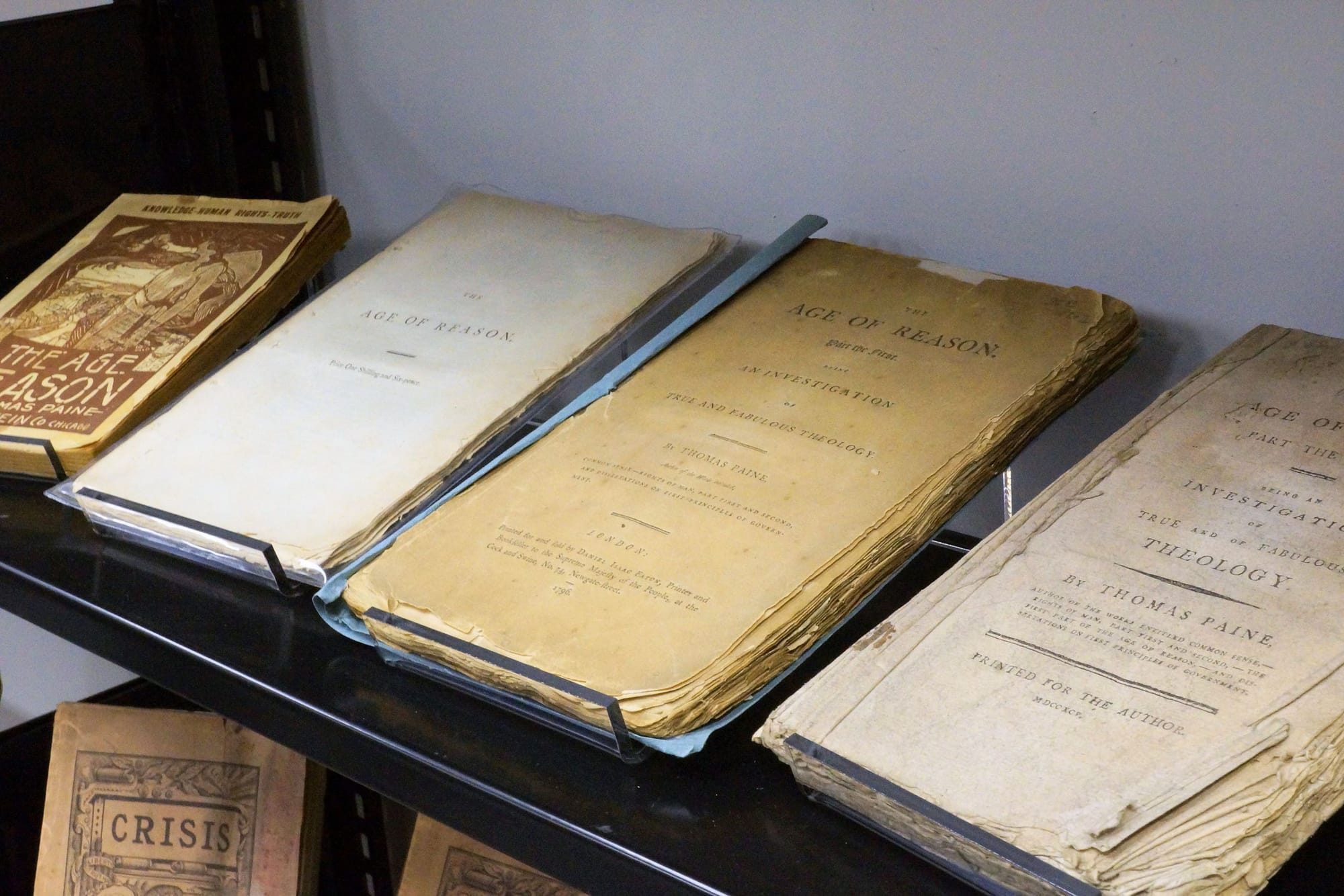Rare editions of Thomas Paine's THE AGE OF REASON in archival boxes, the pages tattered with age. 