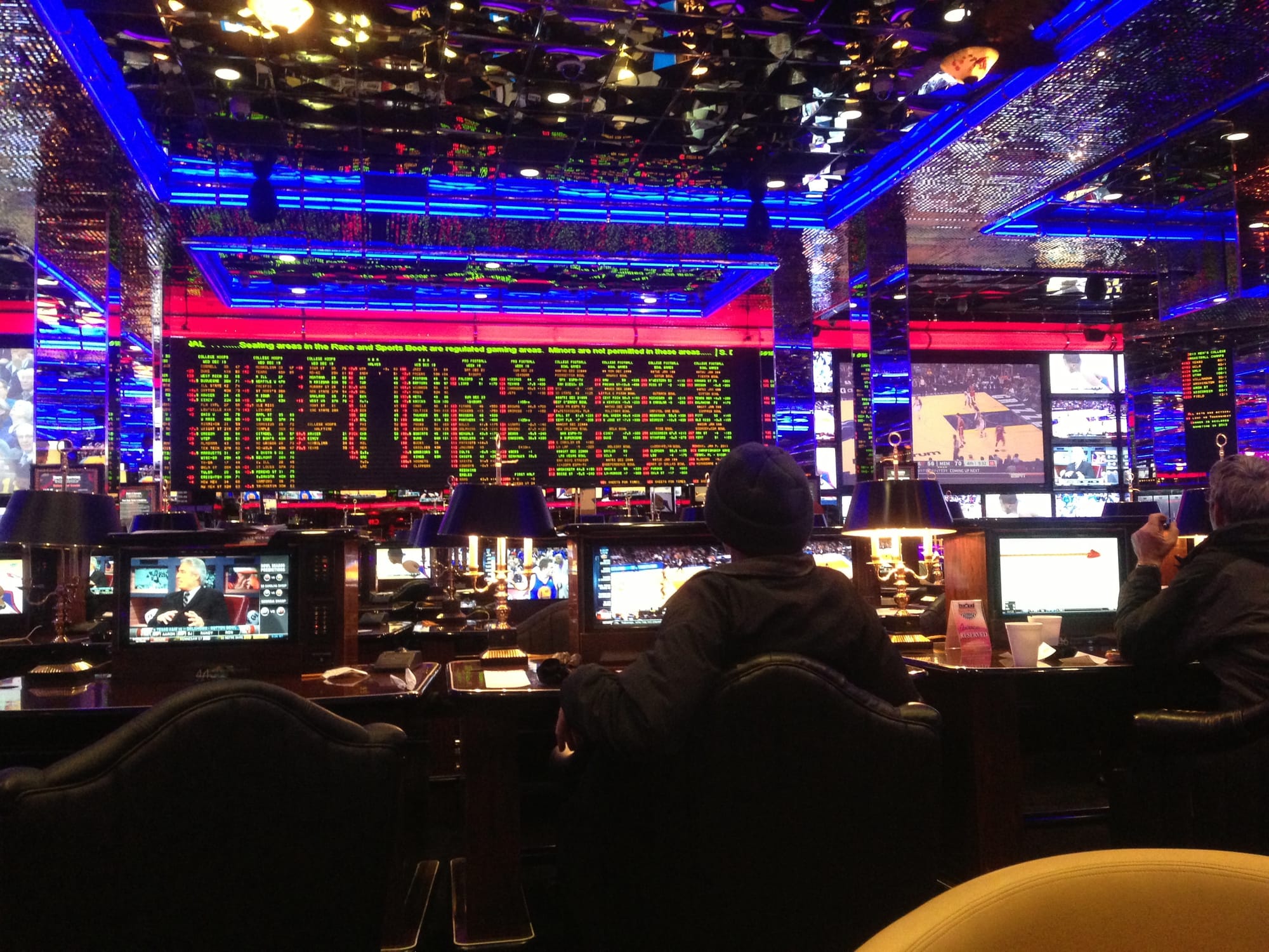 In a darkened casino in Reno, the sports book appears on a huge screen full of complicated text; there's a basketball game in progress on a very small screen off to one side