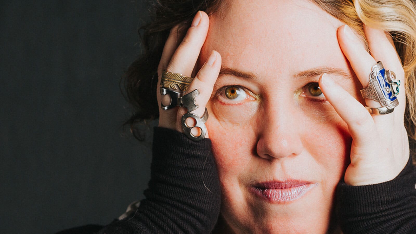 Author Kelly Link in a publicity shot, hands on her cheeks, showing elaborate rings of silver and lapis