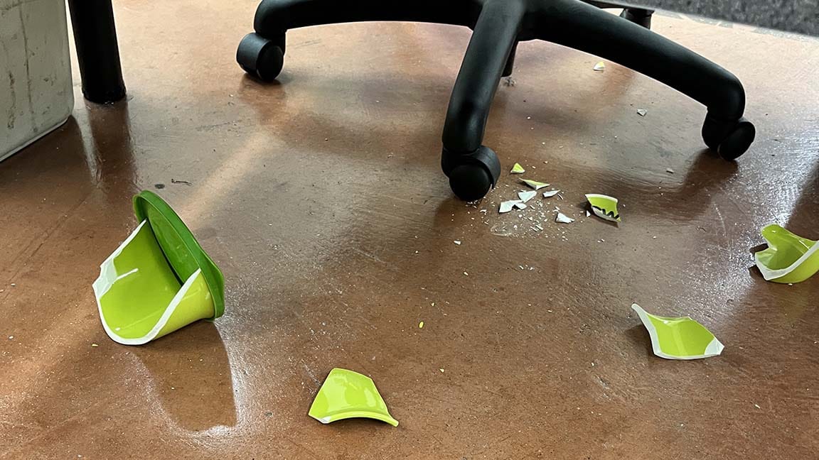 Lime green ceramic soup mug in pieces on floor under desk chair