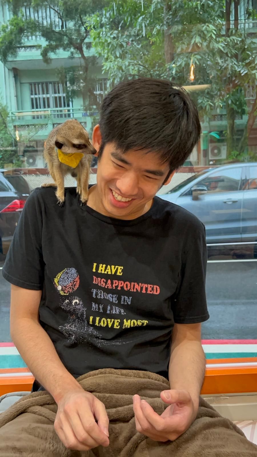 The author visits a meerkat cafe in Taipei and is pictured, laughing, with a meerkat on his shoulder; the meerkat seems to be investigating the author's ear
