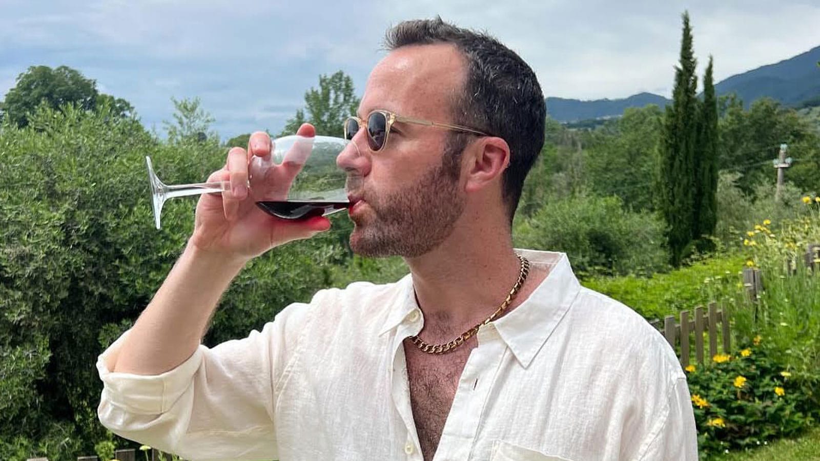 The author in a cream linen shirt and cool sunglasses, enjoying a glass of red wine in the verdant hills of Italy