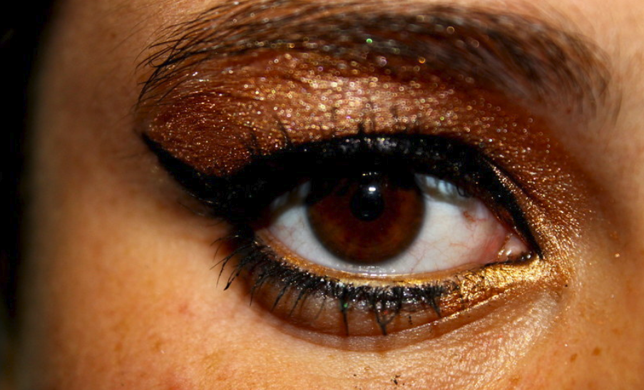 Close up on an eye with artfully applied metallic bronze eyeshadow black mascara and thick black winged eyeliner