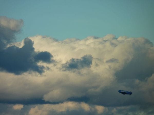 A distant blimp visible against thick clouds, with a rich turquoise sky above