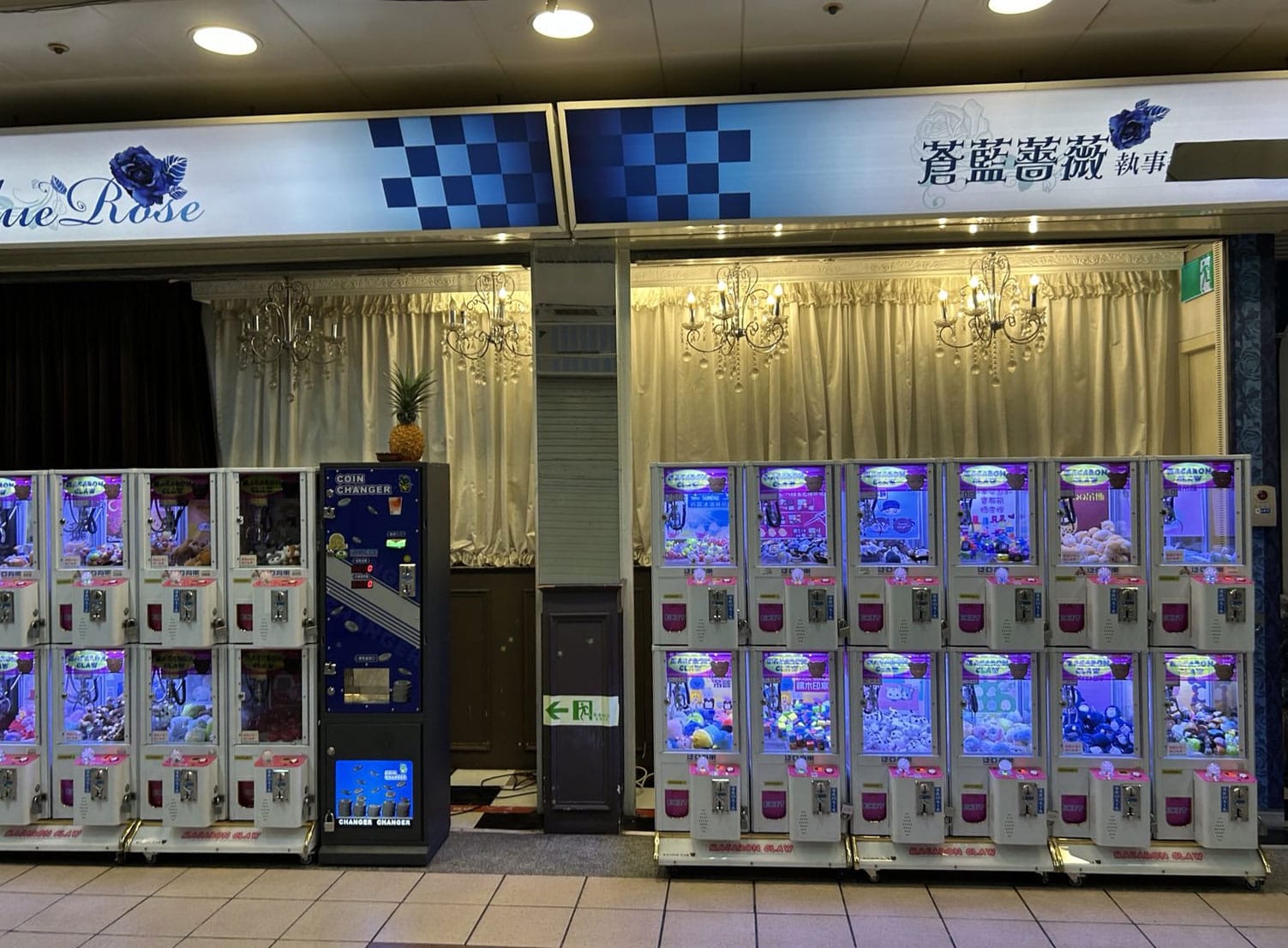 An underground market in Taipei featuring booths draped with chandeliers, banks of colorful toy machines, an artificial pineapple, and a coin changer