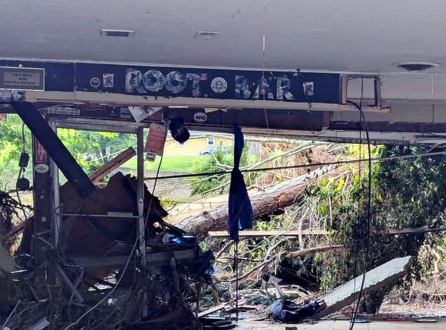 "ROOT BAR spelled out in photographs above a wall that has been washed away; inside and out, fallen trees and debris in thin, milky sunlight