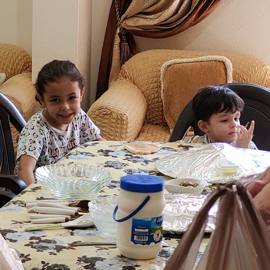 Two children at dinner table, one, smiling, looks directly at camera.