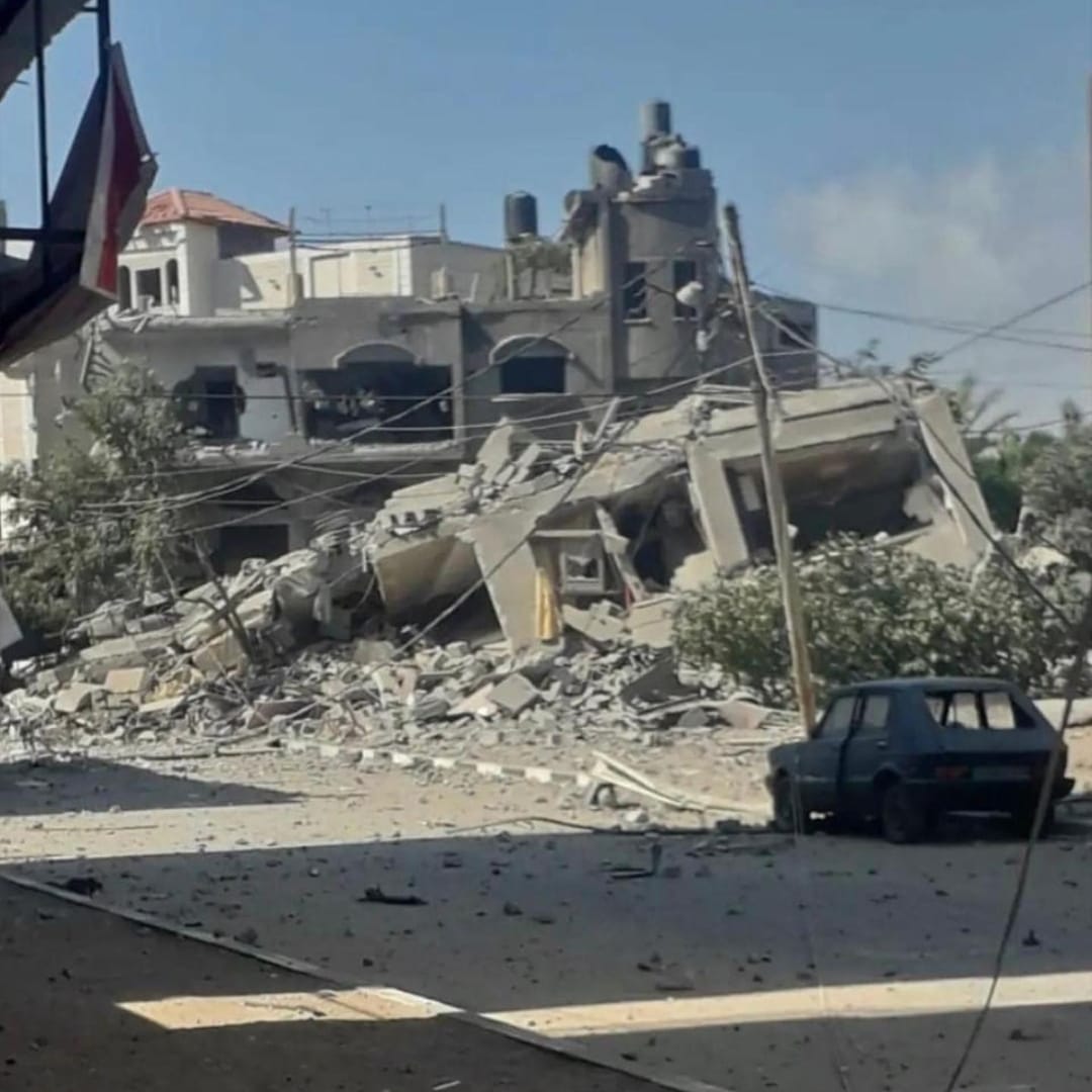 Heavily damaged buildings, a car in foreground with no rear window.