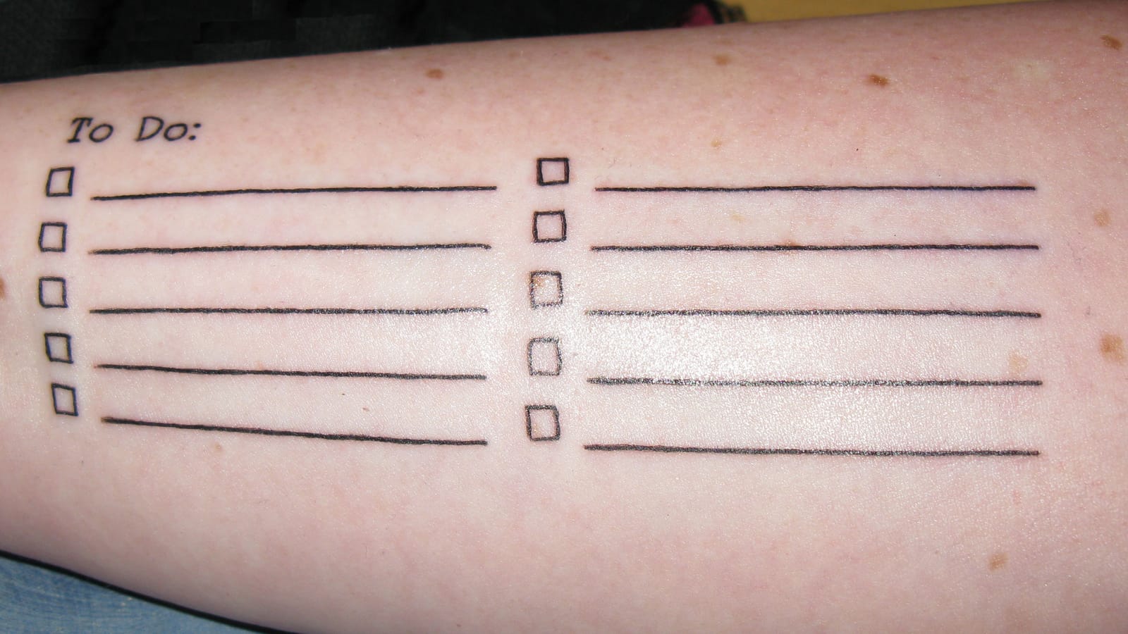 Lightly freckled forearm tattooed with a To Do: list, with ten lines and boxes to check