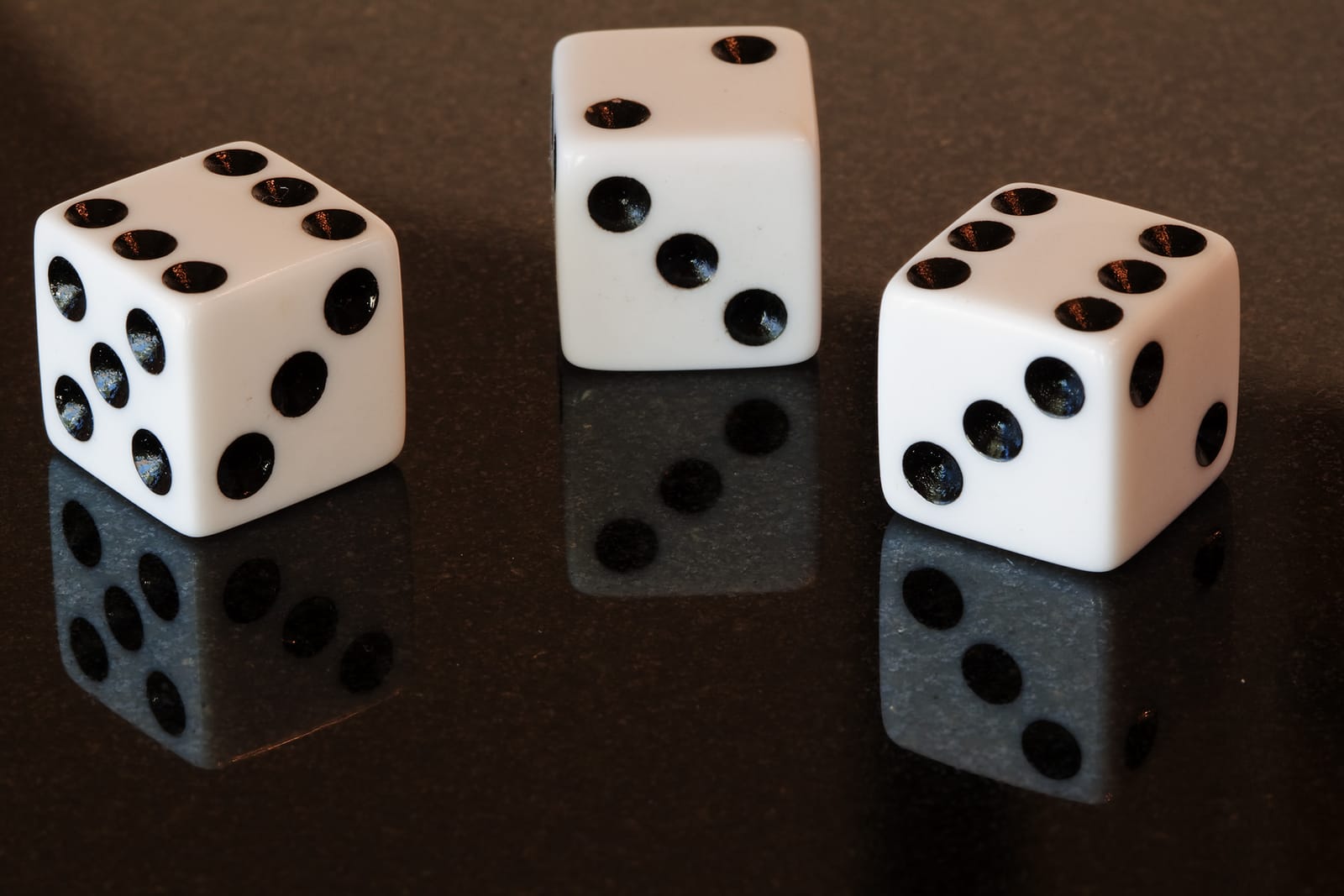 Three white dice on a glossy dark table