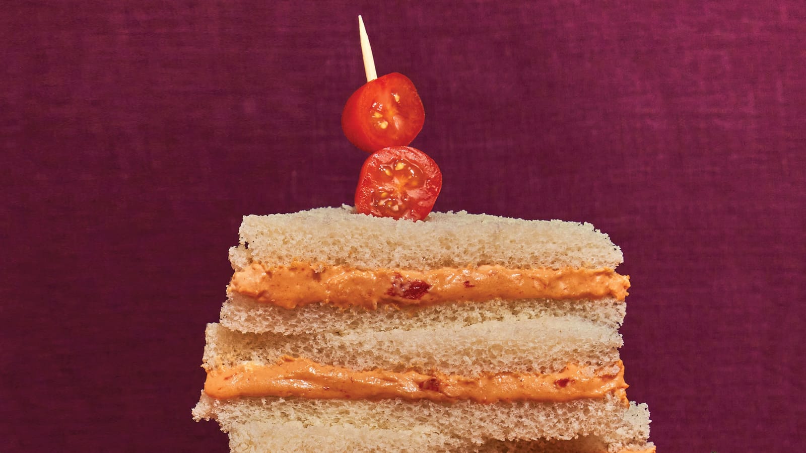 A stack of party sandwiches of meat and cheese-based spread on white bread, with cherry tomatoes on top (recipe below)