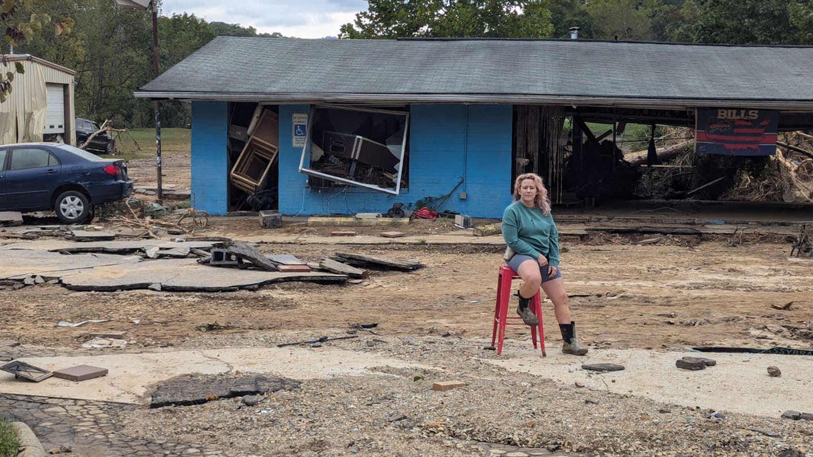 Terri Dolan on a red barstool in front of the remains of the Root Bar after Hurricane Helene