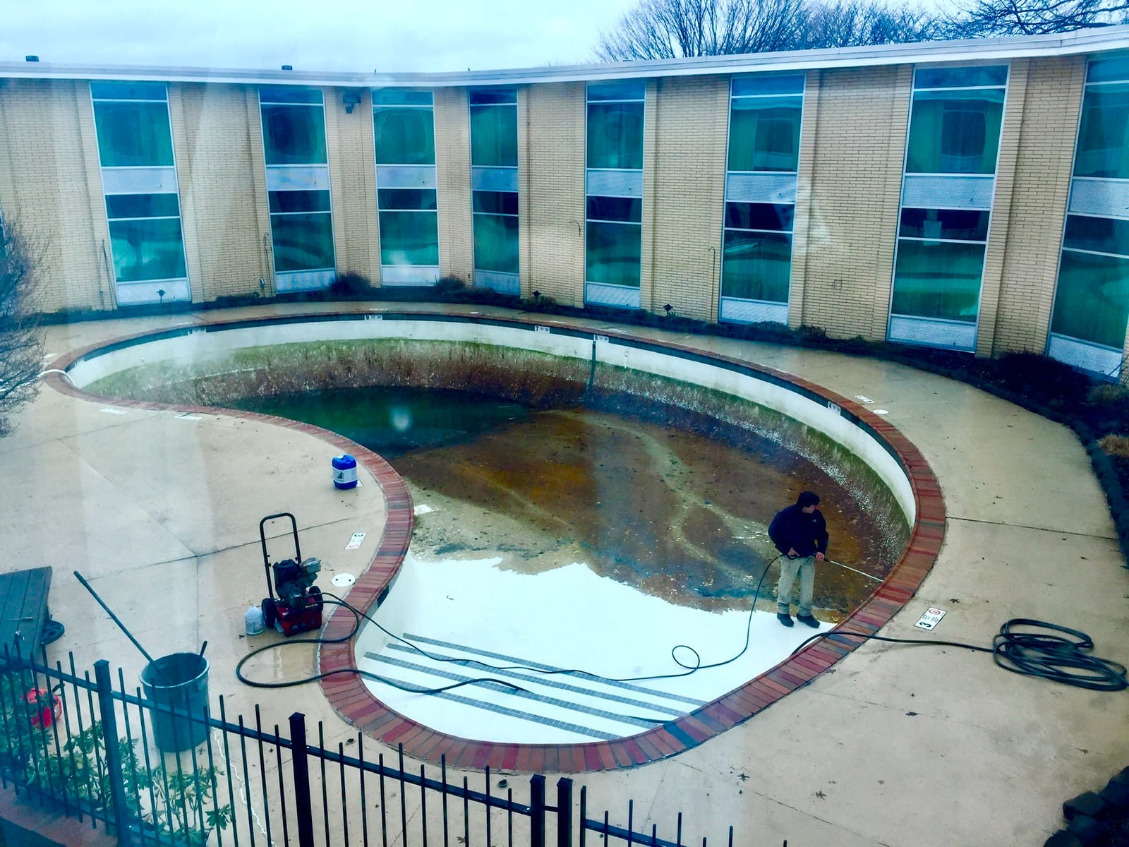 A squat-two story motel with a murky, algae-choked dirty swimming pool, undergoing a cleaning