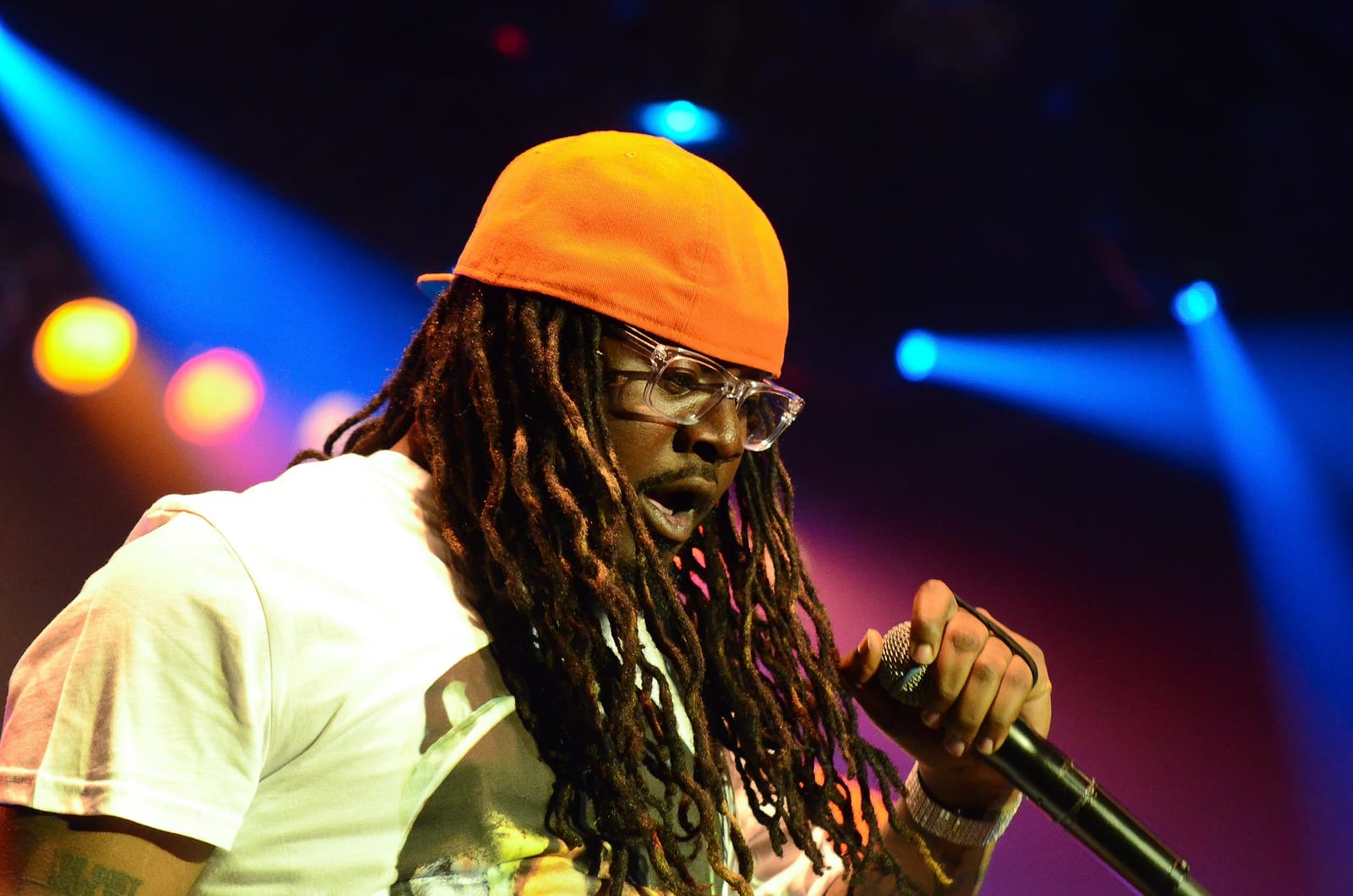 T-Pain onstage in October 2011, wearing clear glasses, long dreads under a tangerine cap, a light t-shirt